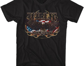 Puede incluir: Camiseta negra con un diseño gráfico de la bandera estadounidense, un águila calva y el nombre "WILLIE NELSON" en letras doradas. El águila tiene las alas extendidas. El diseño está enmarcado por un borde dorado en forma de llama.