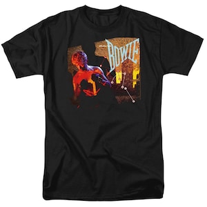Peut inclure: T-shirt noir avec un graphisme coloré représentant une figure et le nom "BOWIE" dans une police stylisée. Le design intègre des tons rouges, oranges et bleus, ainsi qu'une constellation. Le t-shirt a un col rond.