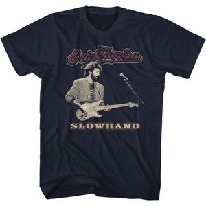 May include: A navy blue t-shirt with a vintage-style image of Eric Clapton playing a guitar. The text "Eric Clapton" and "Slowhand" are printed in red and white on the shirt.