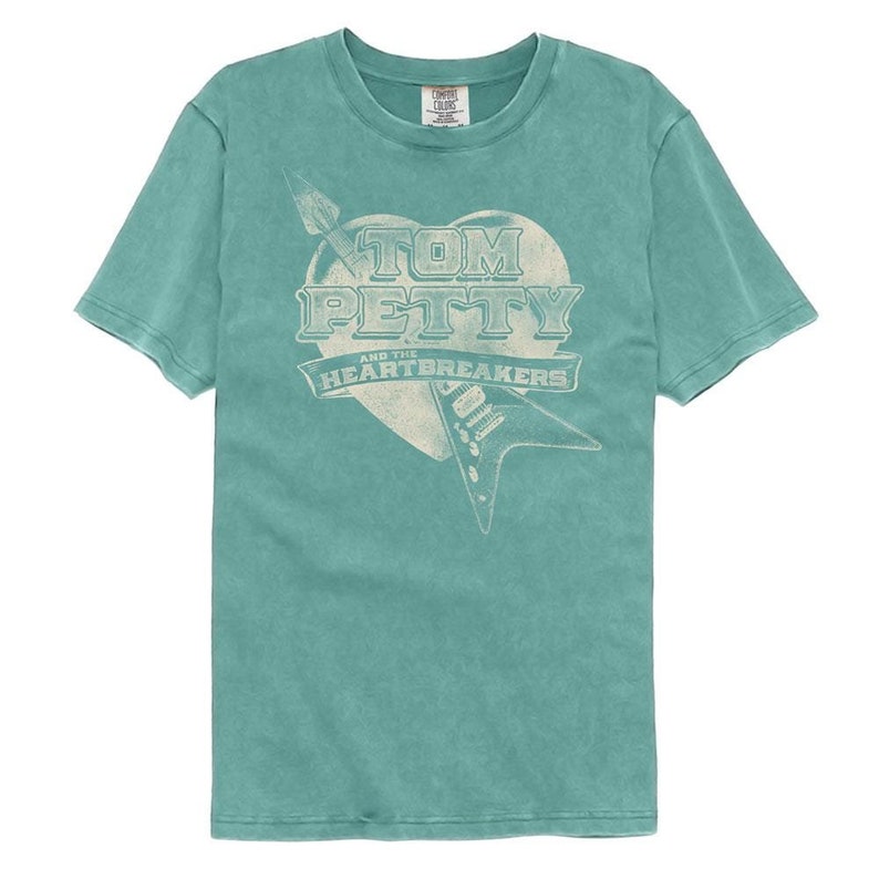 May include: A teal blue t-shirt with a vintage-style graphic of a heart with a guitar and the text "Tom Petty and the Heartbreakers".