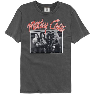 Puede incluir: Una camiseta negra con un aspecto vintage que presenta una foto en blanco y negro de la banda Motley Crue. El nombre de la banda est&aacute; escrito en rojo sobre la foto.