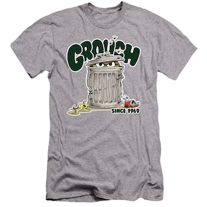 May include: A gray t-shirt with a green "GROUCH" graphic. The graphic features Oscar the Grouch from Sesame Street peeking out of a trash can with the text "SINCE 1969".