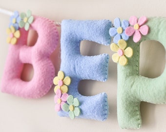May include: A felt banner with the letters "BEP" in pink, blue, and green. Each letter is decorated with felt flowers in various colors.