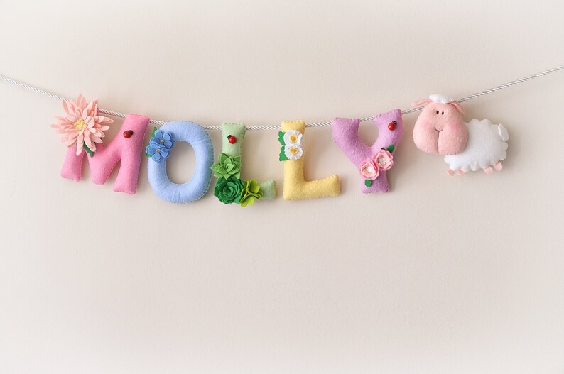 Peut inclure: Une banni&egrave;re en feutre avec le nom "MOLLY" &eacute;crit en lettres color&eacute;es. Chaque lettre est d&eacute;cor&eacute;e de fleurs et d'autres embellissements. Un petit mouton en feutre est attach&eacute; &agrave; l'extr&eacute;mit&eacute; de la banni&egrave;re.