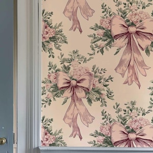 May include: A light blue door with white trim is partially open, revealing a room with wallpaper featuring a repeating pattern of pink bows and floral bouquets on a cream background.