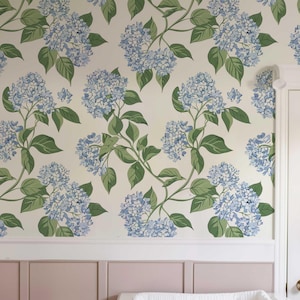 May include: A white changing table with four drawers and gold knobs. The changing table is in a nursery with a pink wall and floral wallpaper.