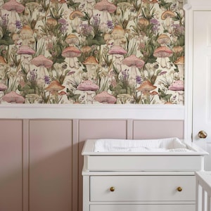 May include: A nursery room with a pink wall and a white changing table with three drawers. The wall is covered in wallpaper with a pattern of pink and orange mushrooms and green foliage.