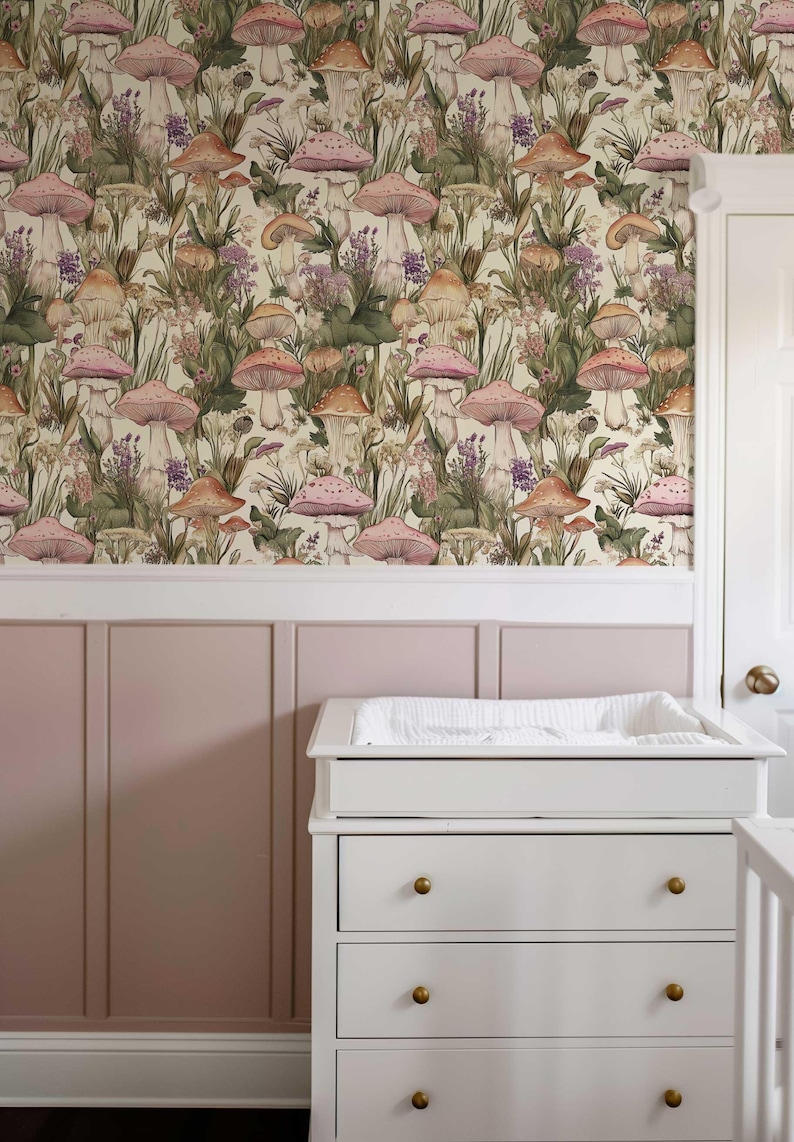 May include: A nursery room with a pink wall and a white changing table with three drawers. The wall is covered in wallpaper with a pattern of pink and orange mushrooms and green foliage.
