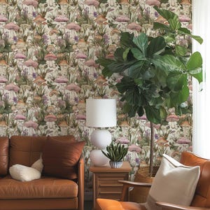 May include: A living room interior featuring a brown leather sofa and armchair, a white lamp, and a large potted plant. The wall is adorned with wallpaper featuring a repeating pattern of pink and brown mushrooms and green foliage.