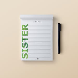 May include: A white notepad with lined pages and the word "notes" in script. The word "SISTER" is printed vertically in green watercolor lettering. A black pen rests beside the notepad.