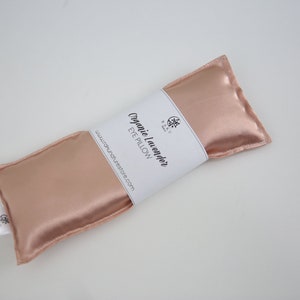 Puede incluir: Una almohada para los ojos de color rosa dorado con una etiqueta blanca que dice "Organic Lavender Eye Pillow" y "www.naturesrestore.com".