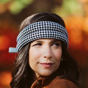 Peut inclure: Un bandeau noir et blanc à motif pied-de-poule. Le bandeau est enroulé autour de la tête. L'arrière-plan est flou avec des couleurs d'automne.
