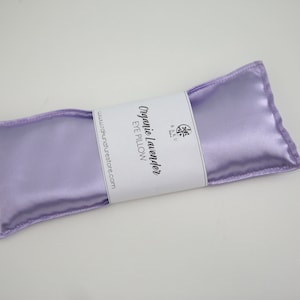 Puede incluir: Una almohada para los ojos de sat&eacute;n lavanda con el texto "Organic Lavender Eye Pillow" y "www.organaturestore.com" impreso en una etiqueta blanca.