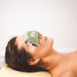 Puede incluir: Una persona acostada de espaldas con una almohadilla para los ojos verde que le cubre los ojos. La persona lleva una toalla blanca y tiene el pelo recogido hacia atr&aacute;s.