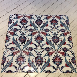 May include: Nine white ceramic tiles arranged in a square, featuring a repeating floral pattern. The design includes red, blue, and teal flowers and leaves. The tiles are likely for decorative use, such as a backsplash or wall accent.