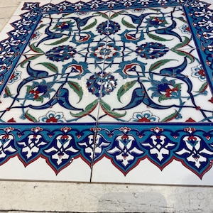 Peut inclure: Ensemble de carreaux de céramique carrés avec un motif floral détaillé. Le motif présente des motifs floraux bleus, rouges et verts sur un fond blanc, encadrés par une bordure bleue avec un motif répétitif. Les carreaux sont assemblés.