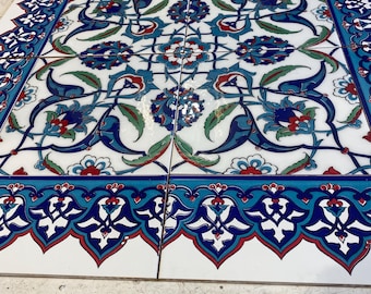 May include: A collection of square ceramic tiles with a detailed floral design. The pattern features blue, red, and green floral motifs on a white background, framed by a blue border with a repeating pattern. The tiles are arranged together.