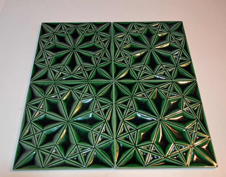 Op de afbeelding: Vier vierkante groene keramische tegels met een geometrisch sterrenpatroon. De tegels hebben een glanzende afwerking en een verhoogd, driedimensionaal ontwerp. Het donkergroene en zwarte kleurenschema cre&euml;ert een opvallend contrast, geschikt voor interieurdecoratie.