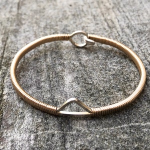 May include: A gold-toned bangle bracelet with a silver triangle accent. The bracelet is made of coiled wire and has a simple, modern design.