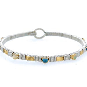 May include: Silver and gold-toned wire-wrapped bracelet with blue and white gemstones. The bracelet has a circular design with a hook clasp. The gemstones are evenly spaced around the bracelet.
