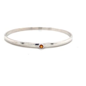 May include: A silver bangle bracelet with a small orange gemstone set in the centre.