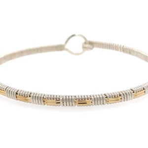 May include: A silver and gold-toned wire-wrapped bangle bracelet. The bracelet features a continuous silver wire with sections of gold-toned wire woven into the design. The bracelet has a circular shape with a small loop closure.