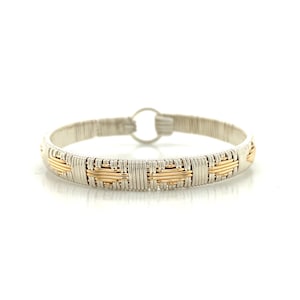 May include: A silver and gold woven wire bracelet. The bracelet has a circular clasp and a repeating pattern of silver and gold wire. The gold wire is woven in a basket-weave pattern. The bracelet is displayed on a white background.