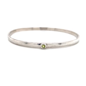 May include: A silver bangle bracelet with a single green gemstone set in the centre.