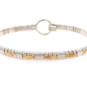 May include: A silver and gold wire wrapped bangle bracelet. The bracelet is made of thin wires that are woven together to create a delicate and intricate design.