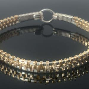 May include: A gold and silver wire-wrapped bangle bracelet with a woven design.