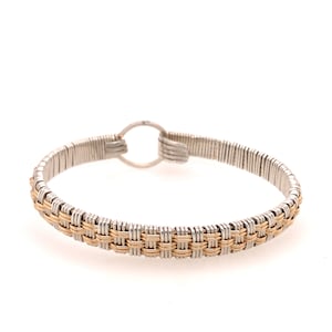 May include: A silver and gold-toned wire-wrapped bracelet. The bracelet features a woven gold-toned centre section and silver-toned wire on the top and bottom. The bracelet has a circular clasp. Jewellery.
