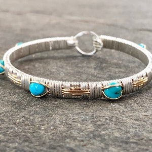 Può includere: Bracciale a cerchio in filo d'argento con perline turchesi. Il bracciale presenta una base in filo d'argento con dettagli in filo d'oro e sei perline turchesi rotonde distanziate uniformemente. La chiusura è un semplice anello d'argento.