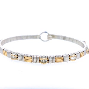 May include: A silver and gold wire-wrapped bracelet. The bracelet features alternating sections of silver and gold wire, with small, clear gemstones set into the gold sections. The bracelet has a simple, elegant design.