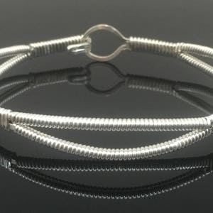 Può includere: Un braccialetto in filo d'argento con un semplice design a cerchio aperto. Il braccialetto è realizzato con due fili di filo intrecciati.