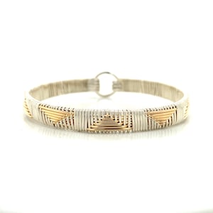 May include: A silver and gold wire-wrapped bracelet. The bracelet features a geometric design with alternating silver and gold sections. The gold sections are square and rectangular shapes. The bracelet has a circular clasp. The overall design is modern and elegant.