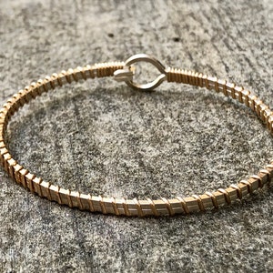 May include: A gold-coloured bracelet with a rectangular link design. The bracelet has a hook clasp and is approximately 17.8 cm in circumference. The jewellery is displayed on a grey, textured surface.