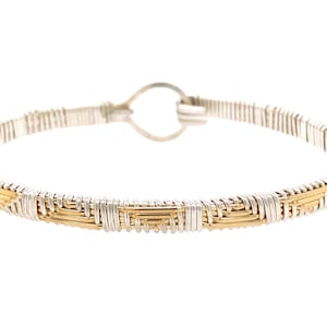 May include: A silver and gold wire-wrapped bangle bracelet with a woven design.