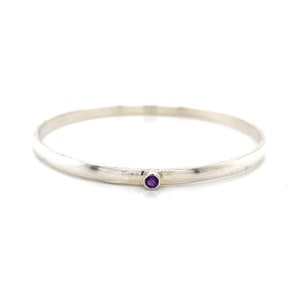 May include: A silver bangle bracelet with a small purple amethyst gemstone set in the centre.