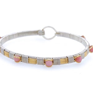 May include: A silver and gold wire-wrapped bracelet with pink gemstones. The bracelet has a circular design with alternating silver and gold wire sections, and small, round pink stones evenly spaced around the band.