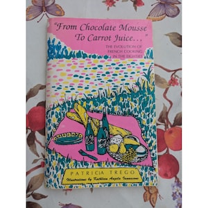 Może przedstawiać: Książka w stylu vintage zatytułowana "From Chocolate Mousse To Carrot Juice..." z różową okładką przedstawiającą scenę piknikową. Okładka zawiera butelki, chleb i talerz. Podtytuł brzmi "The Evolution of French Cooking in the Eighties".