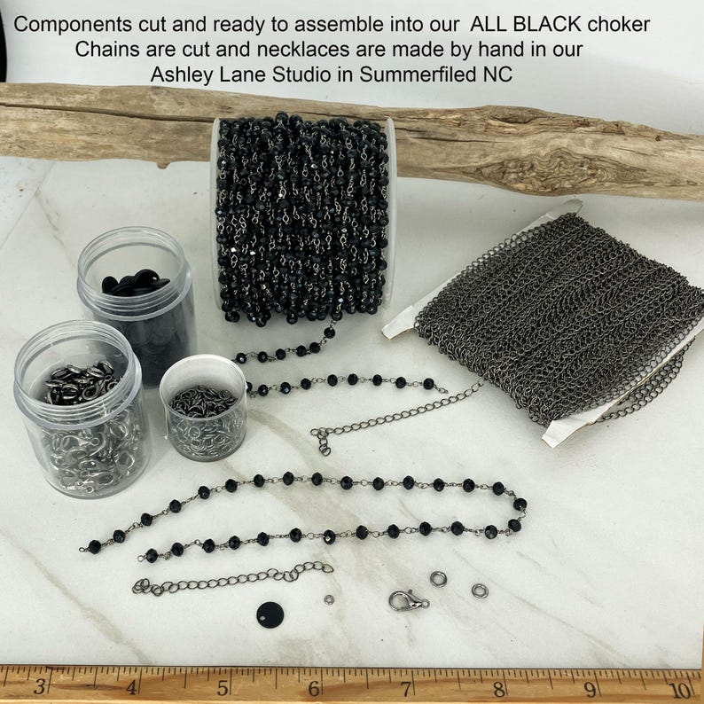 May include: Components for an all black choker including a spool of black beaded chain, a spool of dark metal link chain, three clear plastic jars containing metal clasps and rings, and loose chain segments with a ruler showing 10 inches.