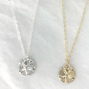 May include: Two delicate necklaces with a sand dollar pendant. One necklace is silver and the other is gold.