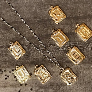 May include: A gold chain necklace with nine gold charms, each featuring a different letter of the alphabet. The letters are K, H, I, L, J, A, S, E, and U.