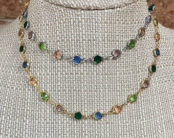 May include: Two layered necklaces with colorful gemstone accents. The top necklace is silver with a light pink, green, and blue color scheme. The bottom necklace is gold with a light pink, green, and blue color scheme.