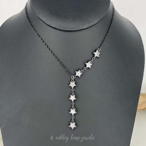 May include: A black chain necklace with a silver star pendant. The necklace has a Y-shaped design with stars cascading down one side.