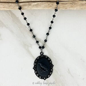 May include: Black beaded necklace with a black cameo pendant featuring a bird design. The cameo is set in a decorative filigree frame.