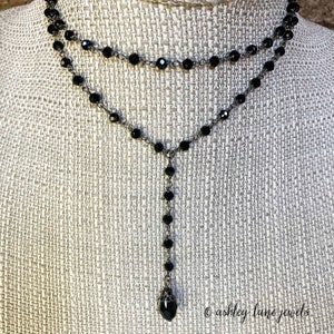 May include: A black beaded necklace with a teardrop pendant. The necklace is layered and has a delicate chain.