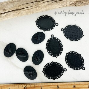 May include: A collection of eight black metal cameo pendants, including six with intricate filigree designs and two with raised bird motifs.  The pendants are arranged on a white surface with a wooden ruler in the foreground.