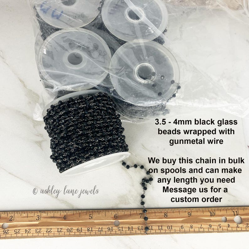 May include: A spool of black glass beads wrapped with gunmetal wire, measuring 3.5 - 4mm. The text reads: 3.5 - 4mm black glass beads wrapped with gunmetal wire. We buy this chain in bulk on spools and can make any length you need. Message us for a custom order.