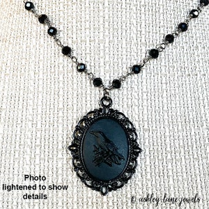 May include: Black necklace with a black cameo pendant featuring a bird design. The pendant is surrounded by a decorative filigree frame.